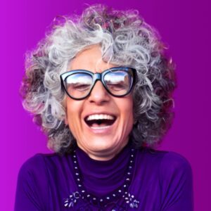 A grey-haired woman smiling against a vibrant purple background.