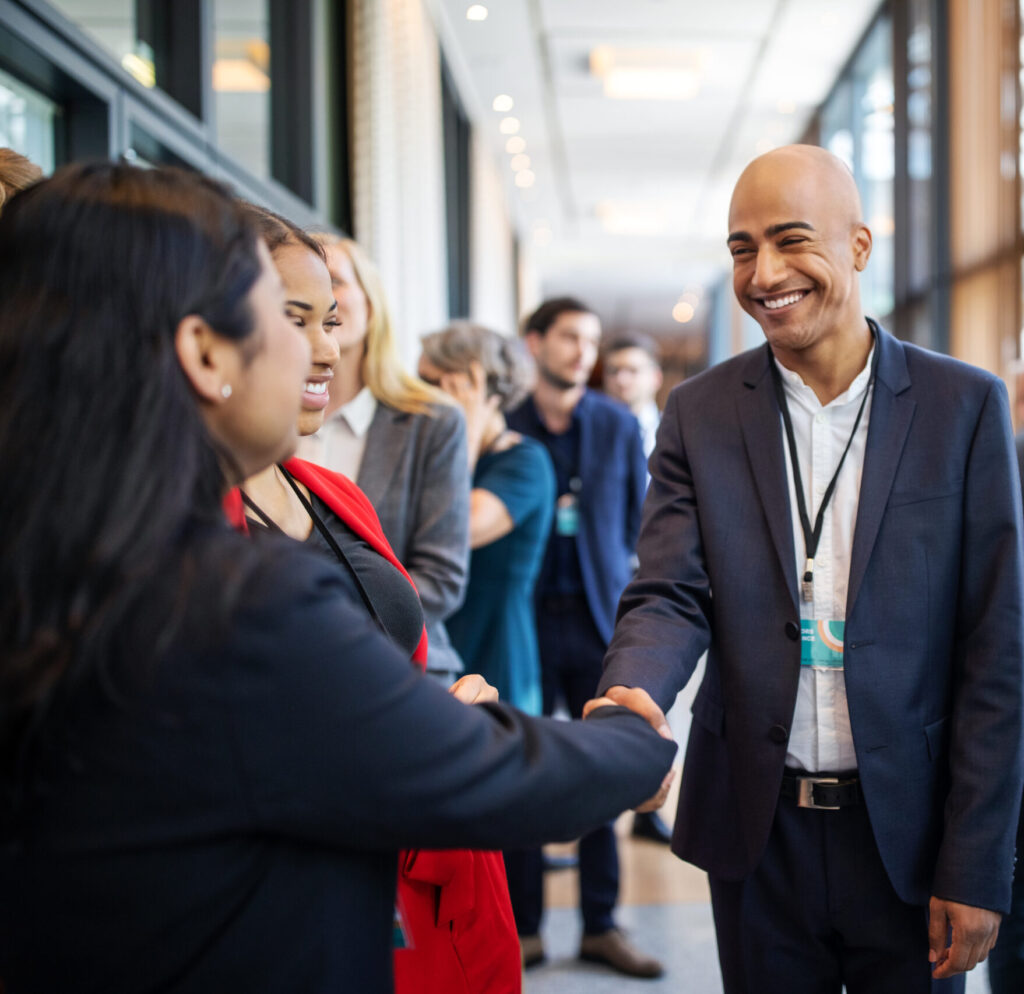Business executives in hotel corridor handshaking during coffee break. Male and female professionals are standing in corridor. They are attending launch event in hotel.